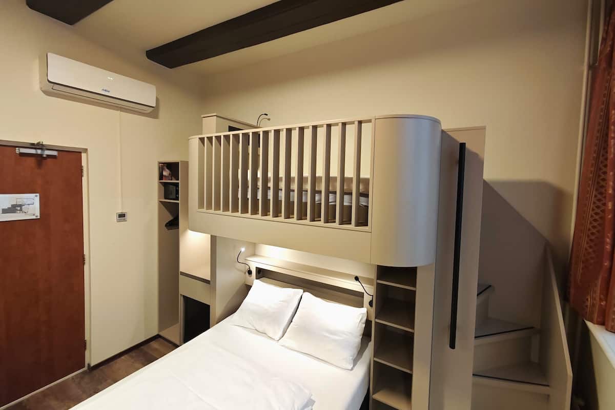 Quarto de hotel compacto com uma cama beliche, escrivaninha embutida e guarda-roupa.