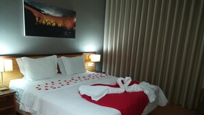 A hotel room with a neatly made bed, a painting on the wall, and a window with blinds. - Hotel Dom Vilas (Braga)