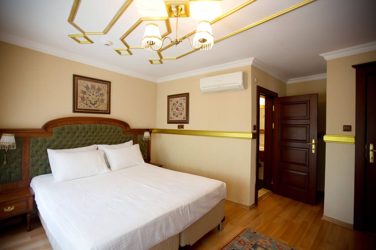 Une chambre d’hôtel avec un grand lit, une tête de lit en bois, deux lampes fixées au mur et une porte donnant sur une autre pièce.