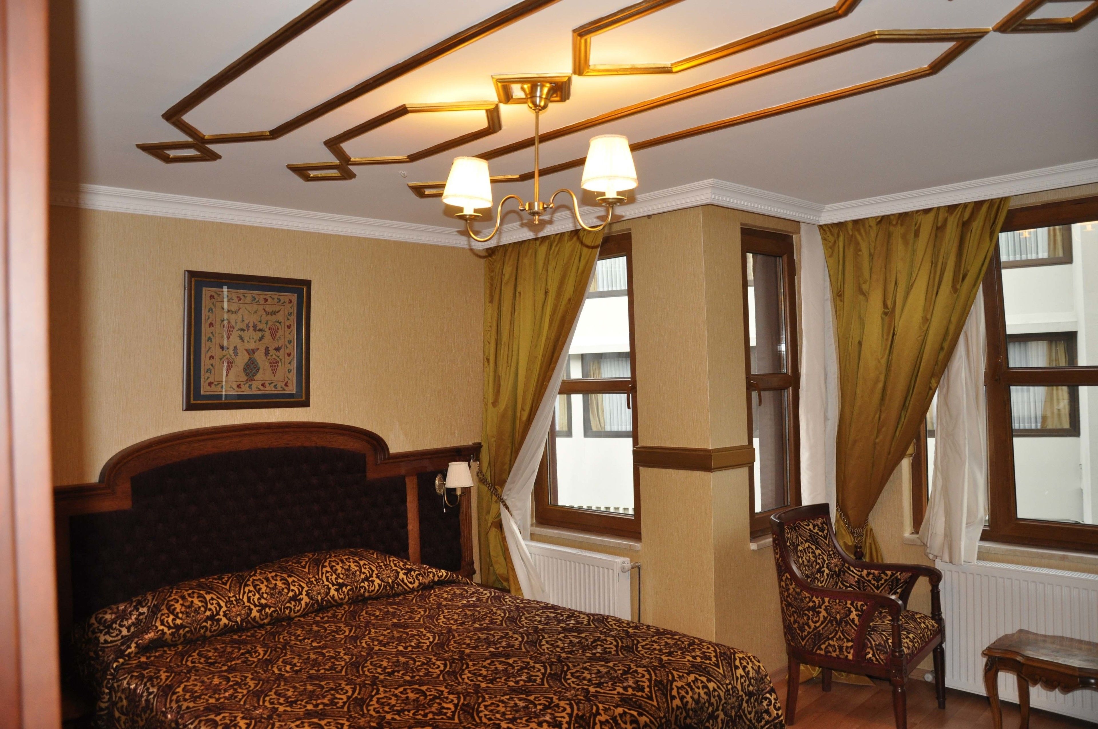 A hotel room with a patterned bedspread, a wooden headboard, a chair, a table, and a chandelier.