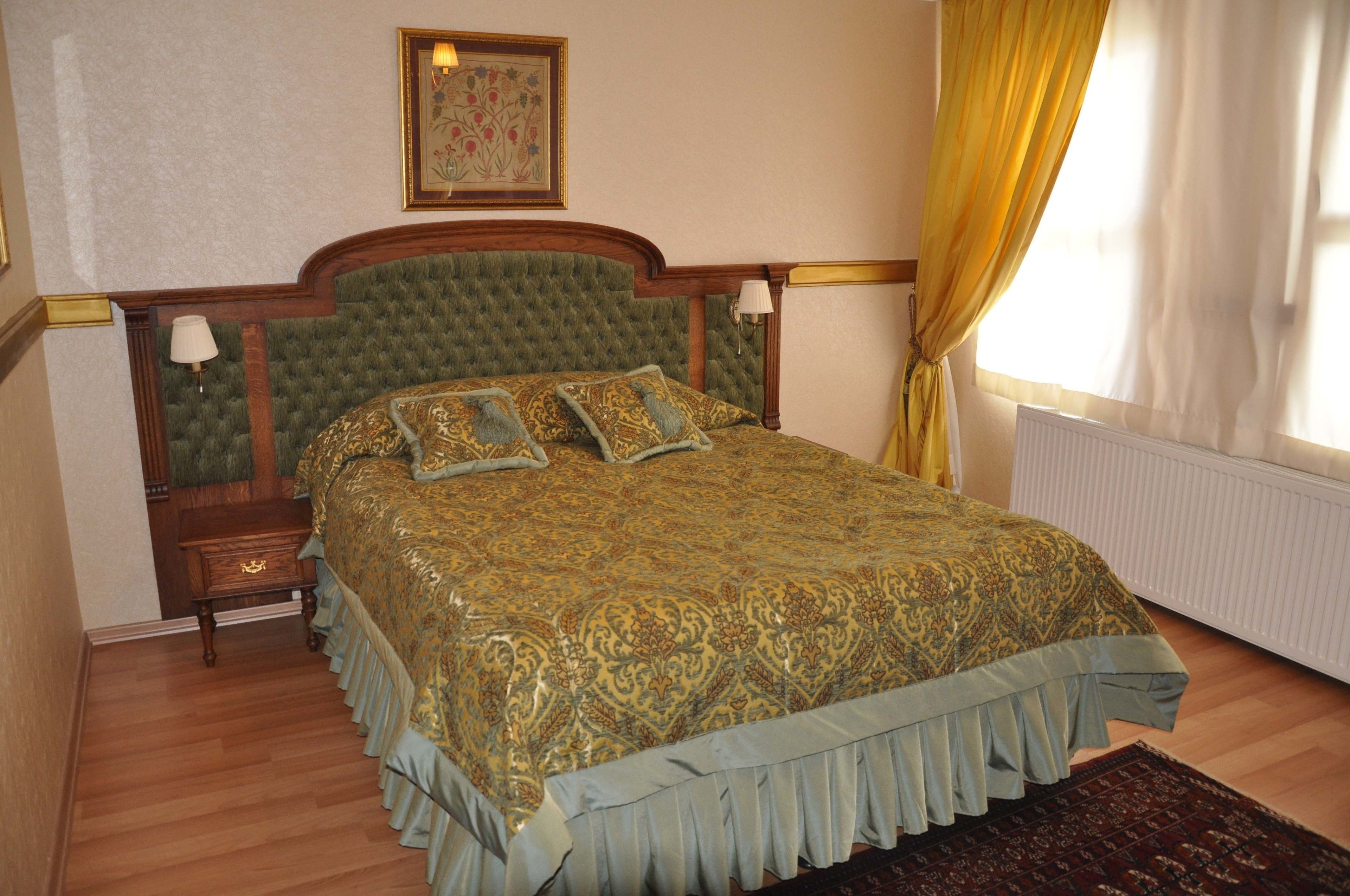 A bedroom with a large bed, wooden headboard, two bedside tables, a nightstand, a framed picture on the wall, and a window with curtains.