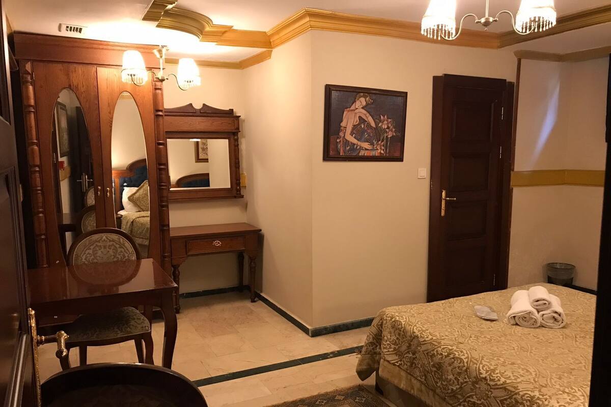 Une chambre d’hôtel avec un lit, un bureau doté d’un miroir, une chaise, un tapis et un tableau au mur.
