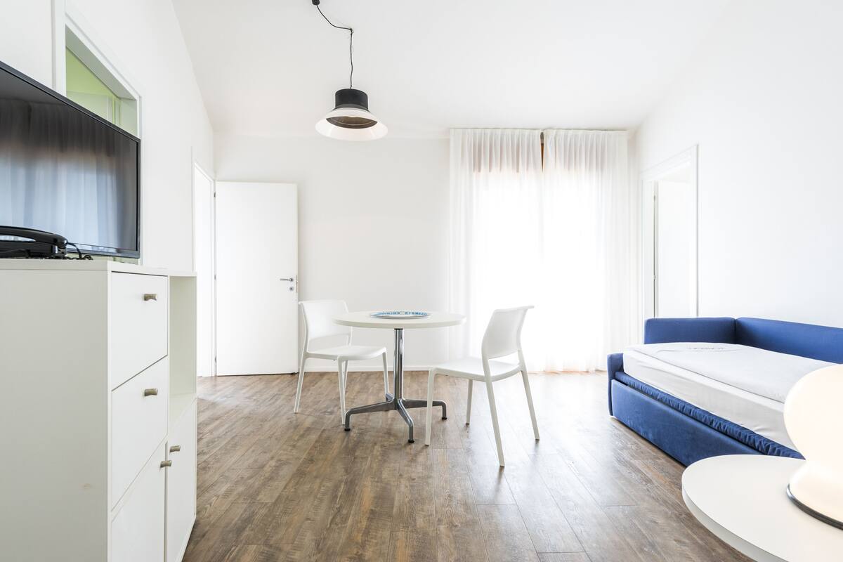 A modern, minimalistic room with a wooden floor, white furniture, a round table, and a blue sofa.