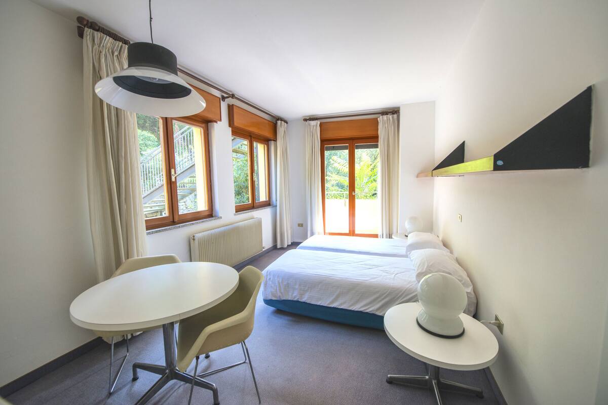 A hotel room with a bed, a round table, a chair, a desk, and a lamp.