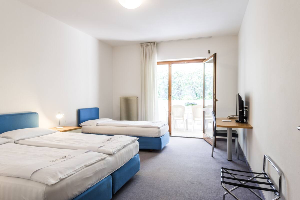 A hotel room with two beds, a desk, a chair, and a radiator.