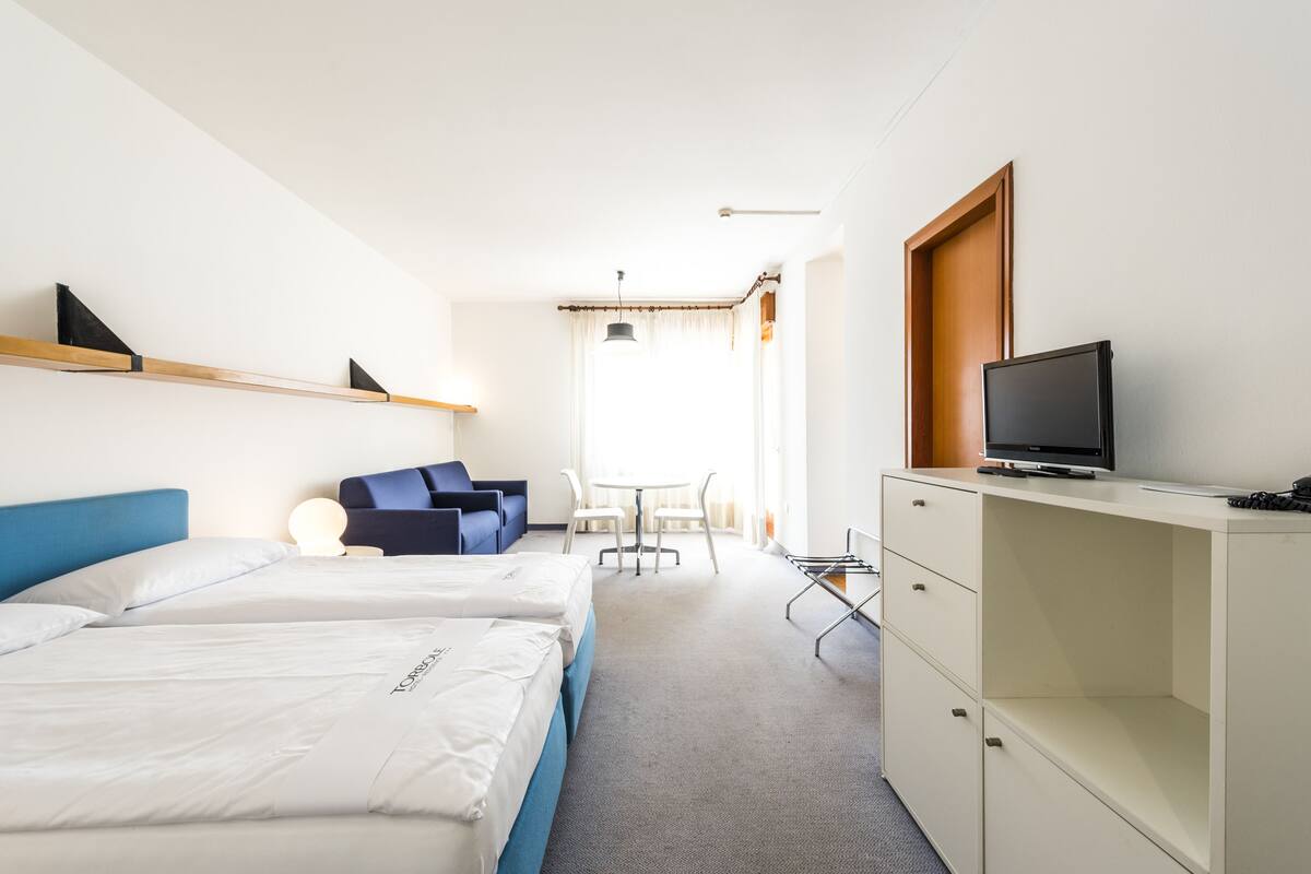 A hotel room with two beds, a desk, a television, and a seating area with chairs and a table.