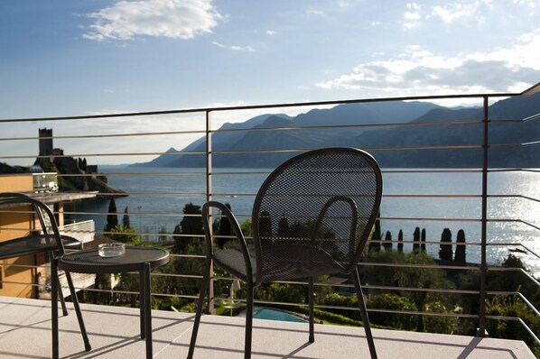 Een balkon met twee stoelen en een tafel met uitzicht op een meer en bergen.