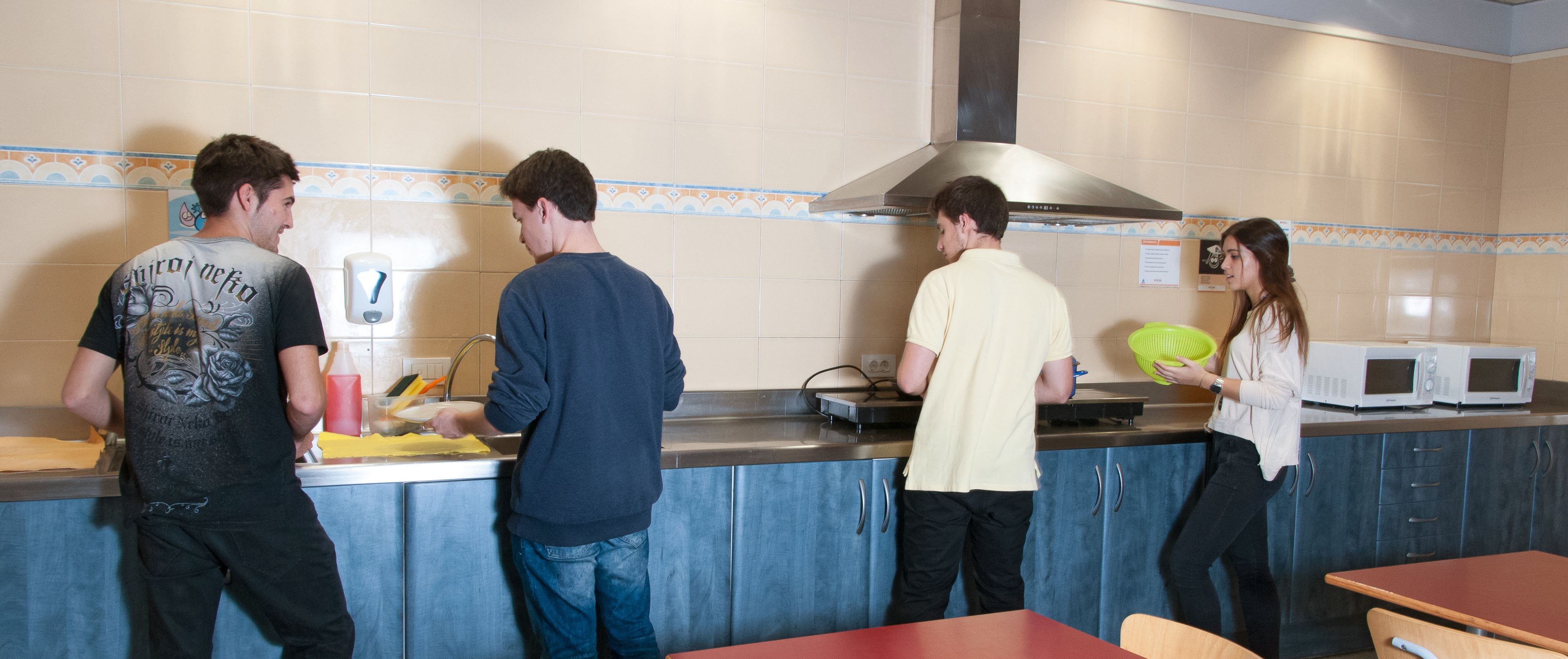 Een keuken met vier personen, een spoelbak, een fornuis en een magnetron.