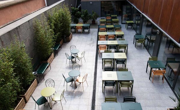 A spacious outdoor patio with multiple tables and chairs, surrounded by greenery and a stone wall. - Barcelona Pere Tarrés Hostel (Barcelona)