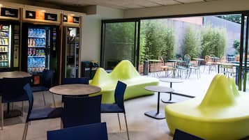 A modern indoor seating area with tables and chairs, a vending machine, and a view of the outdoor patio.