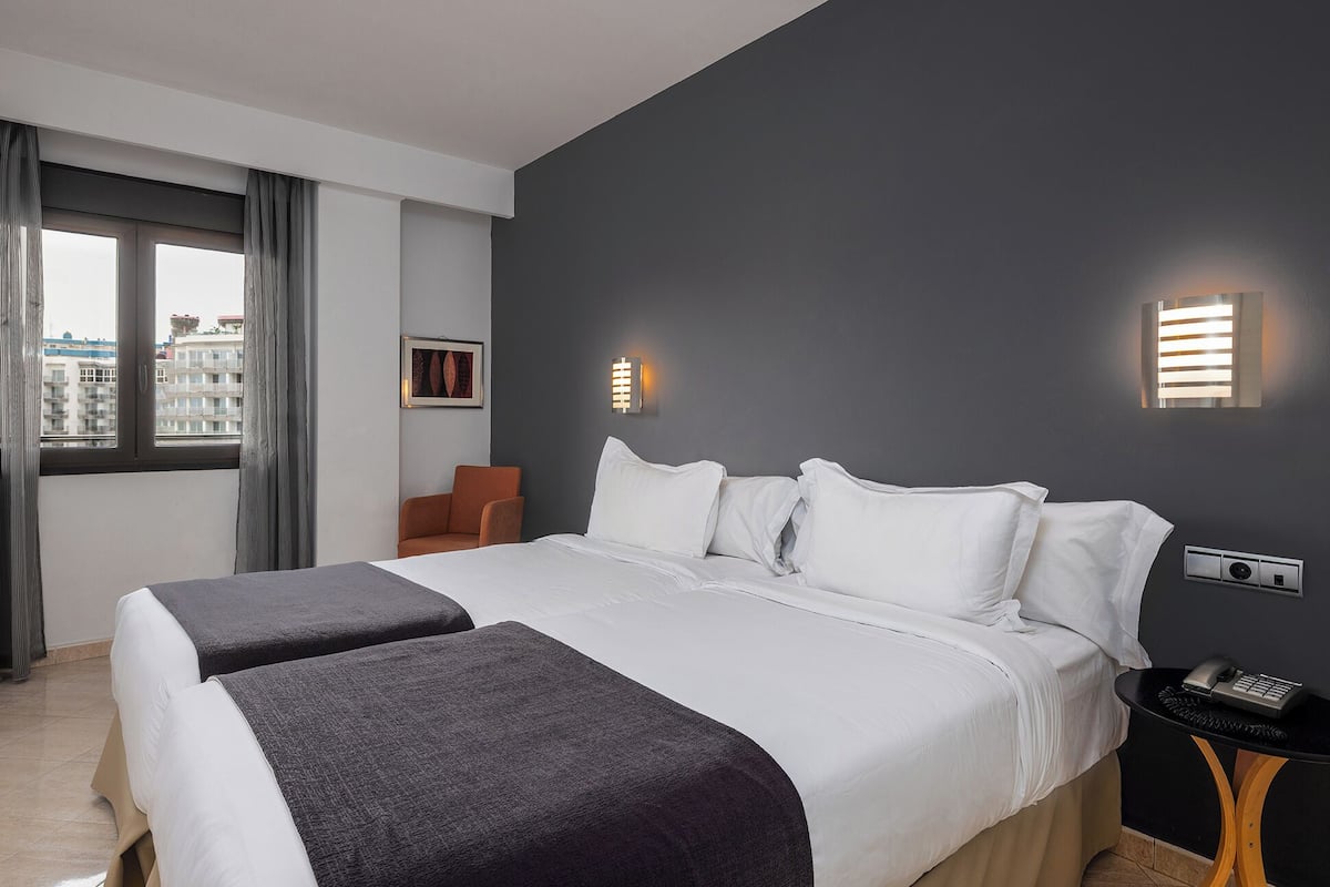 A hotel room with a large bed, two bedside tables, a chair, and a window with curtains.