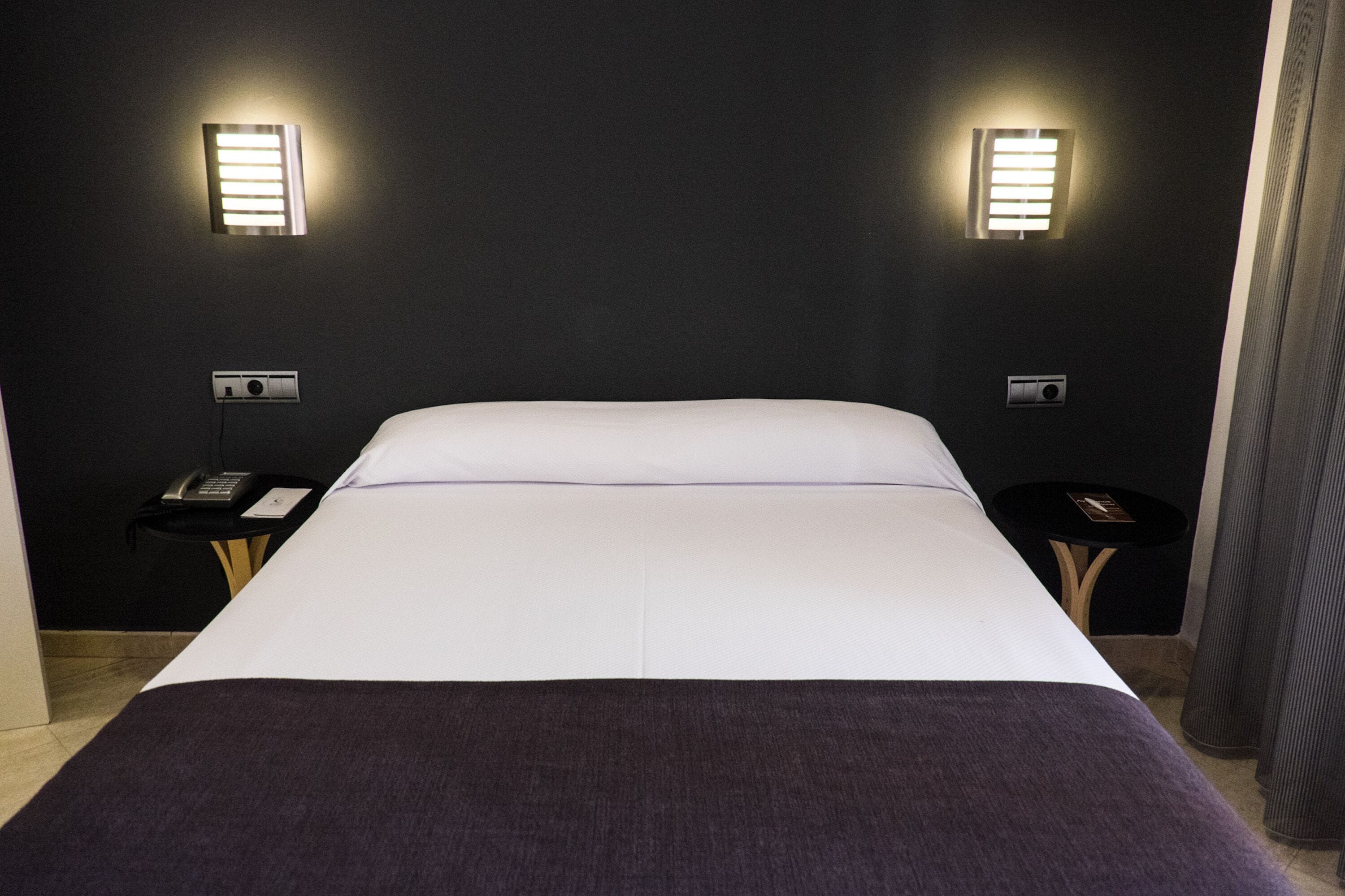 A hotel room with a large bed, two bedside tables, a telephone, and wall-mounted lights.
