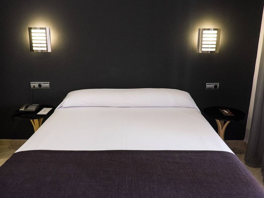 Camera d'albergo con un letto grande, due comodini, un telefono e luci a parete.