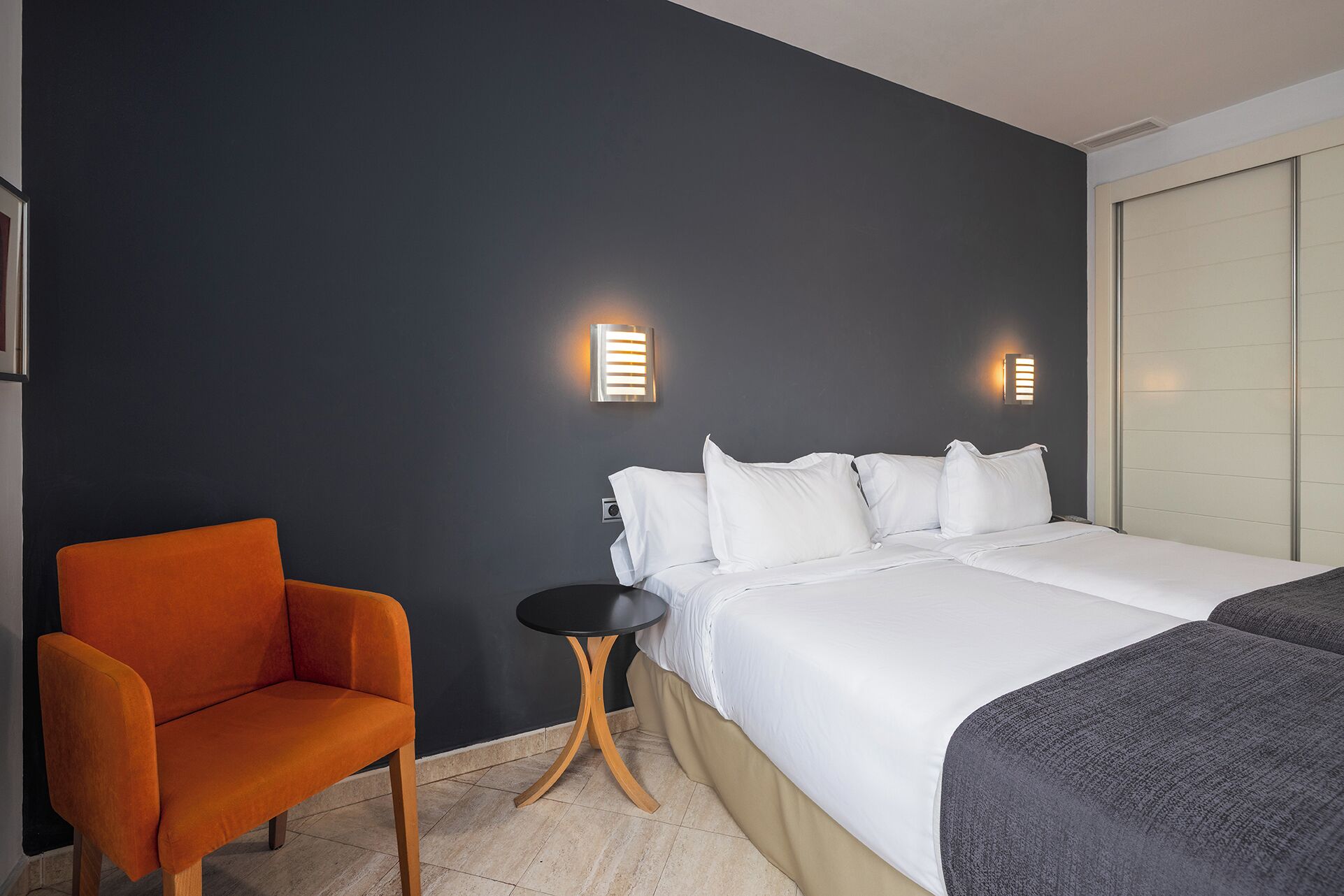 A hotel room with a bed, a small round table, and an orange chair.