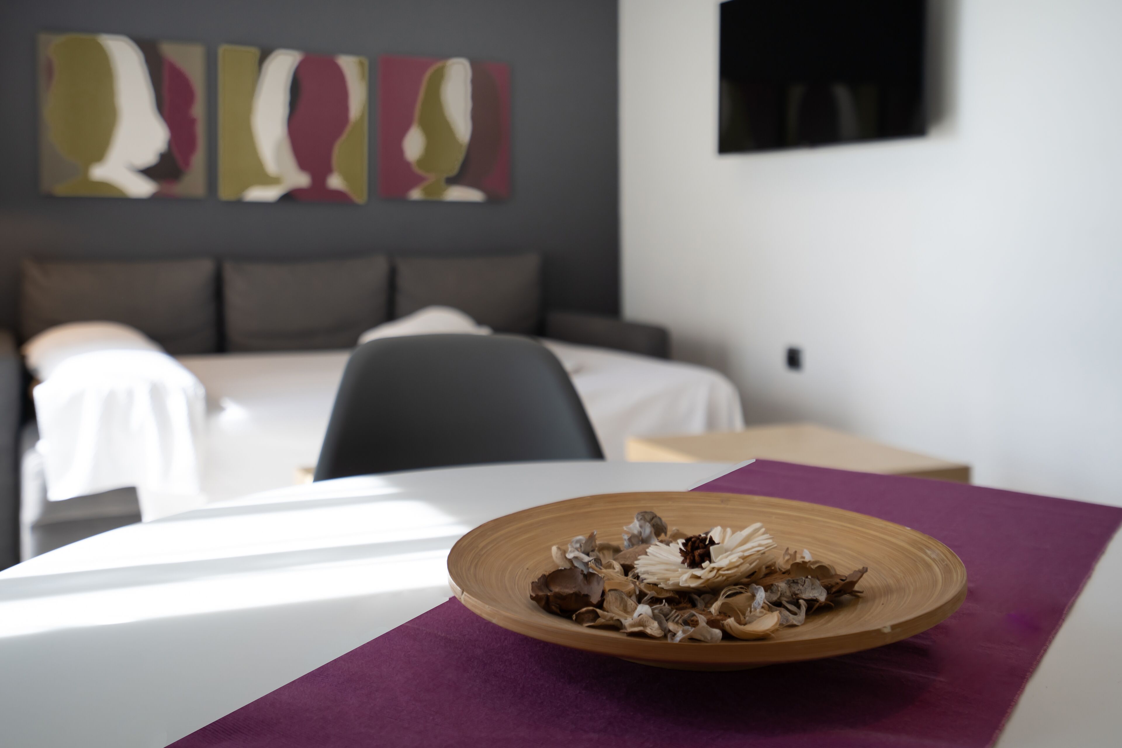 Een hotelkamer met een bed, een nachtkastje en een decoratief bord op een paarse tafelonderzetter.