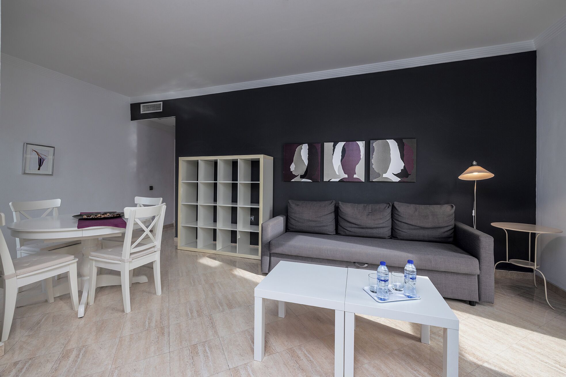 Un salón moderno con una mesa blanca, un sofá gris y un armario blanco.