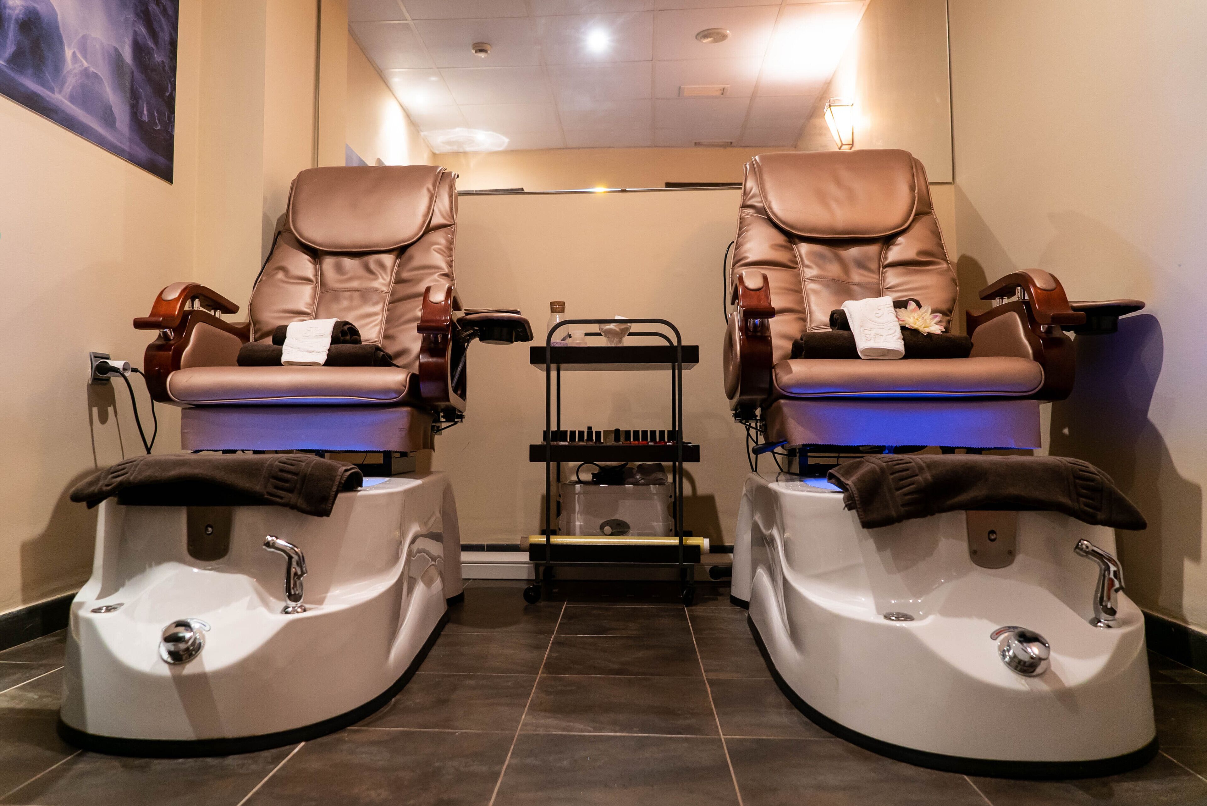 Um quarto com duas cadeiras de massagem, uma mesinha com uma toalha e uma bacia para os pés.