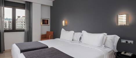 Habitación de hotel con una cama grande, dos mesitas de noche, una ventana con cortinas y vistas a la ciudad.