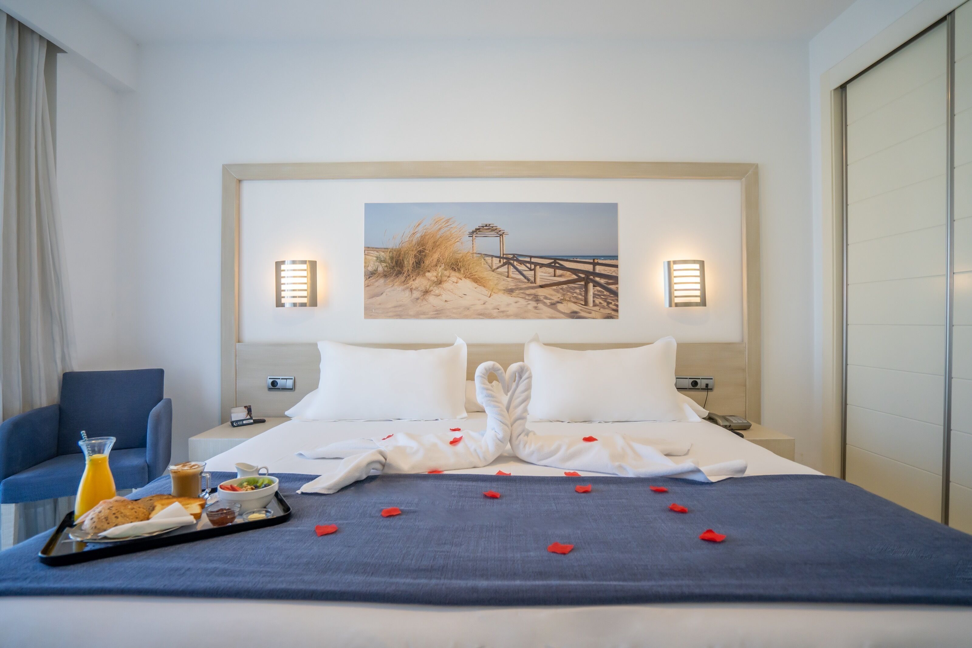 A hotel room with a bed, a breakfast tray, and a beach scene painting on the wall.