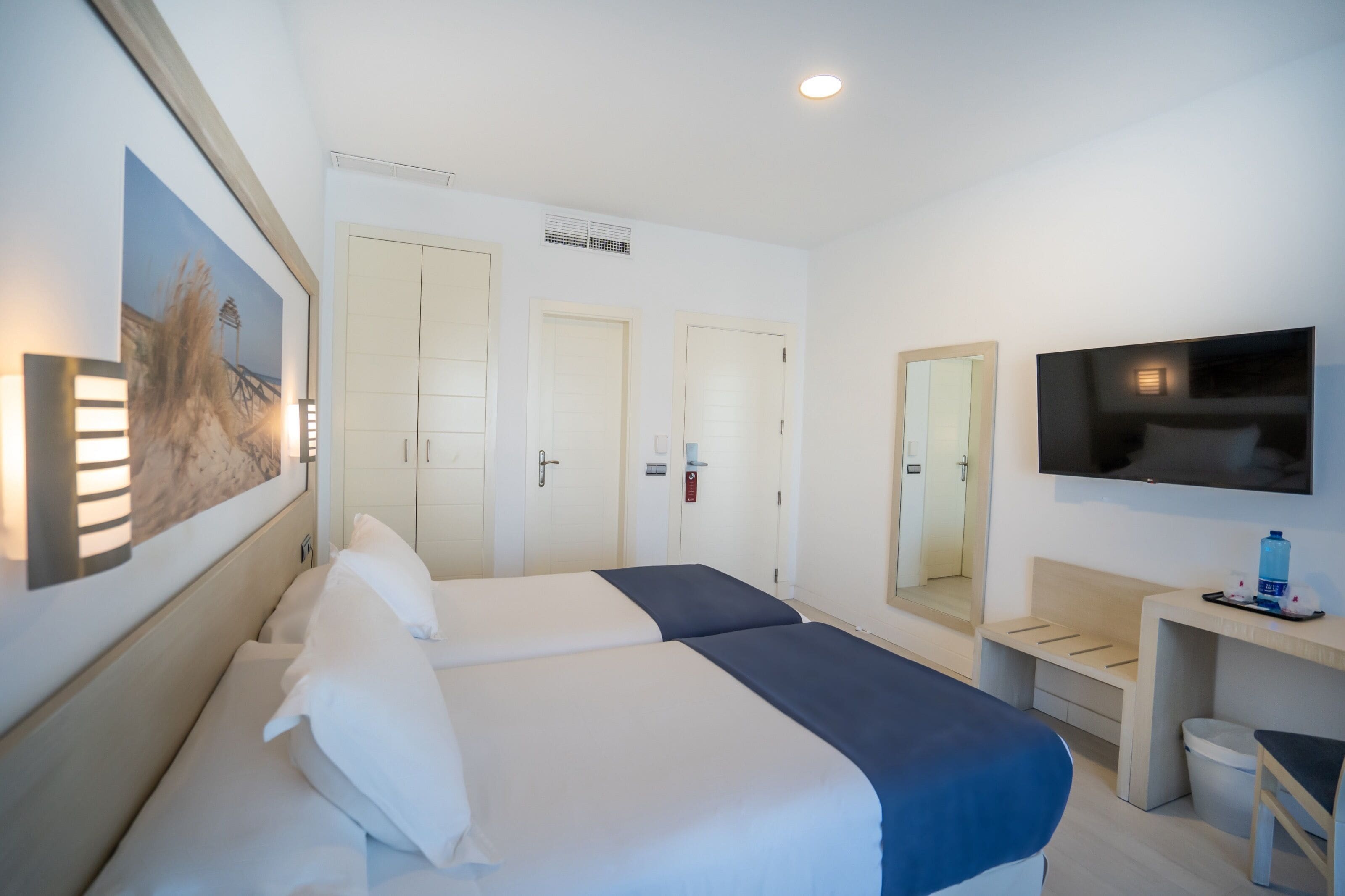 Ein Hotelzimmer mit zwei Betten, einem Schreibtisch, einem Fernseher und einem Bild an der Wand.