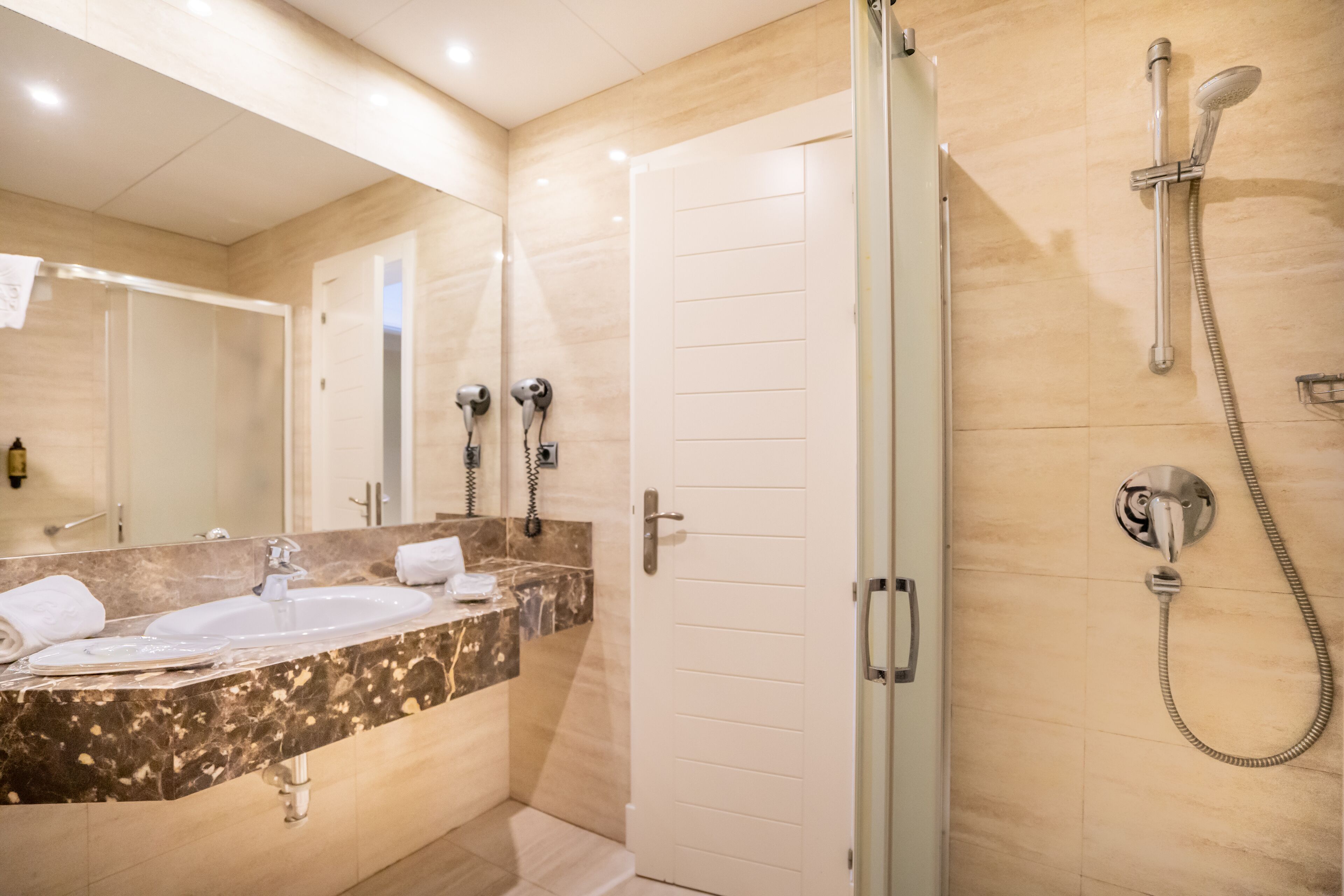 Un baño moderno con ducha envuelta en vidrio, lavamanos de mármol y un espejo grande.