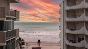 Un hotel frente a la playa con varios balcones que dan al océano, una torre de salvavidas y una vista despejada del atardecer.