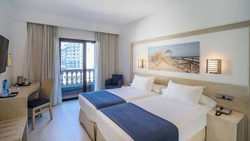 Hotelkamer met twee bedden, een bureau, een stoel, een televisie, een balkon met gordijnen en een schilderij aan de muur.