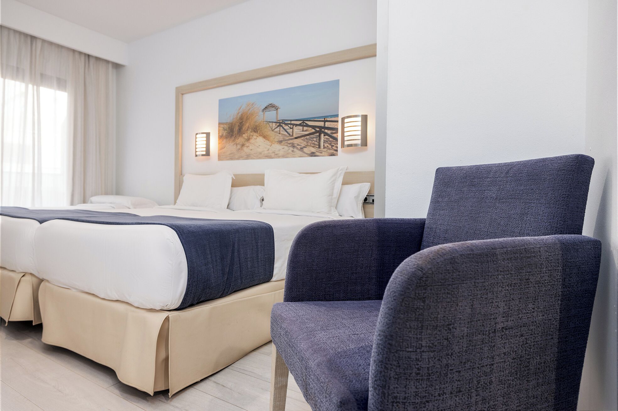 Een hotelkamer met een bed, twee fauteuils, een schilderij aan de muur en een raam met gordijnen.