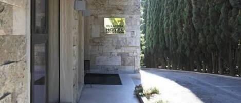 A stone building with a covered outdoor area, a sign indicating a hotel, and a row of tall trees.
