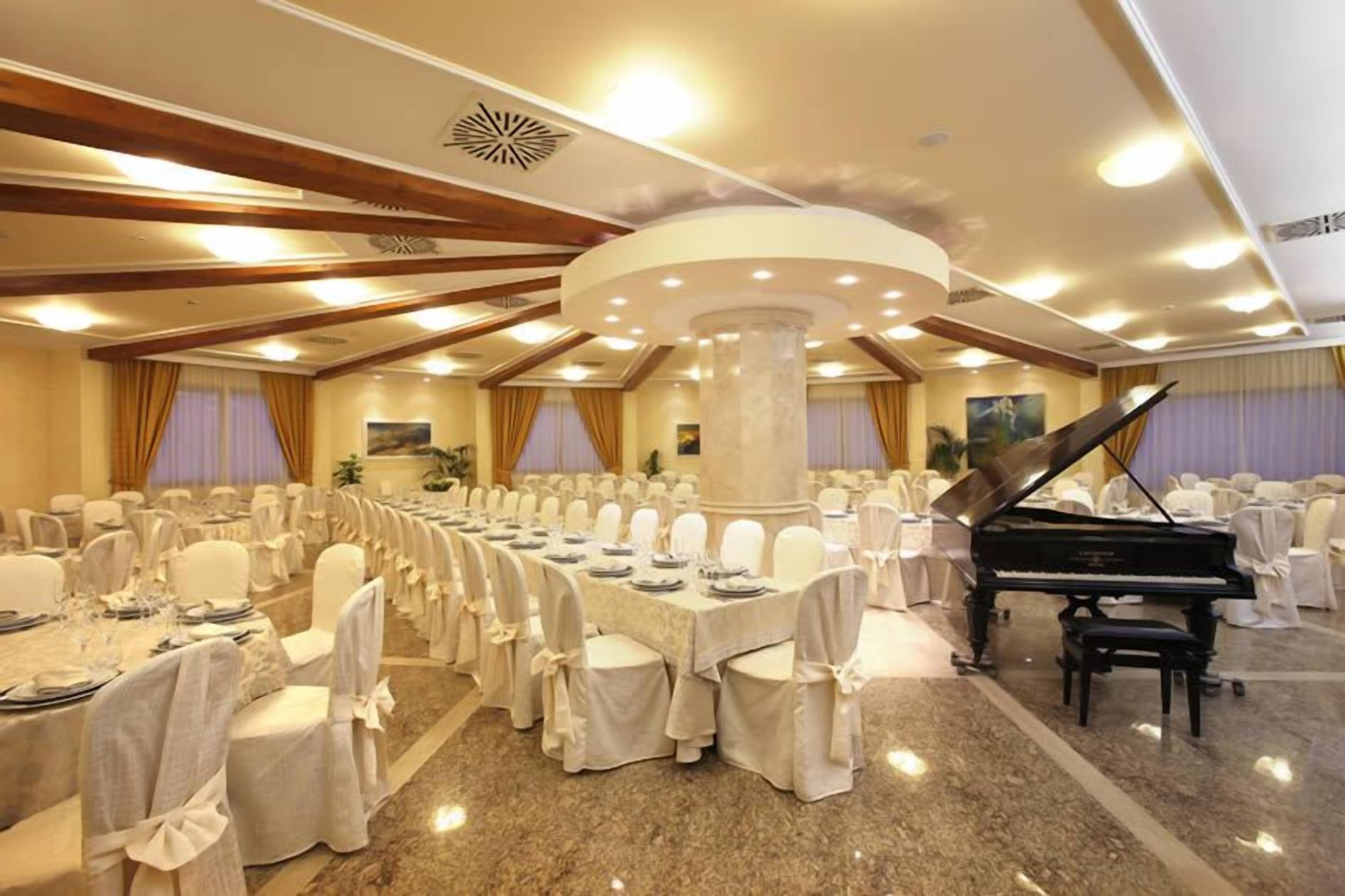 A banquet hall with round tables, white chairs, and a grand piano.