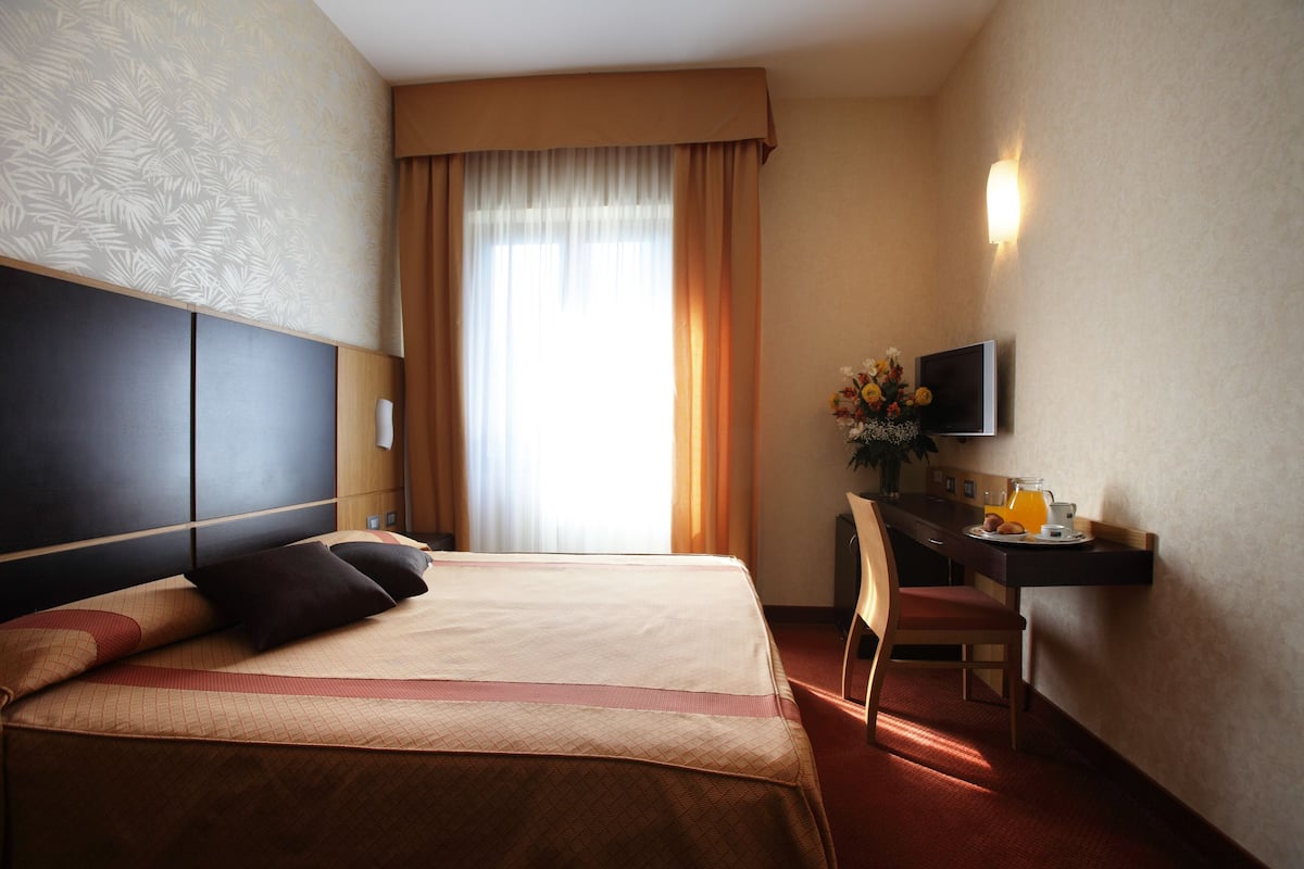 A hotel room with a large bed, a desk with a TV, and a window with curtains.