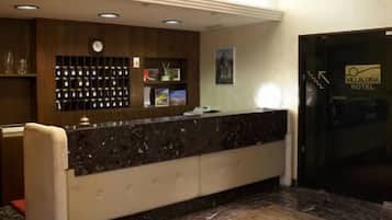 Ein Hotel-Empfangsbereich mit Marmorboden, einer Rezeption, einer Kristallleuchtre und einer Wanduhr.