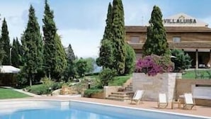 A swimming pool with lounge chairs, surrounded by tall trees and a building labeled "VILLA ALUISA". - Villa Luisa (Todi)