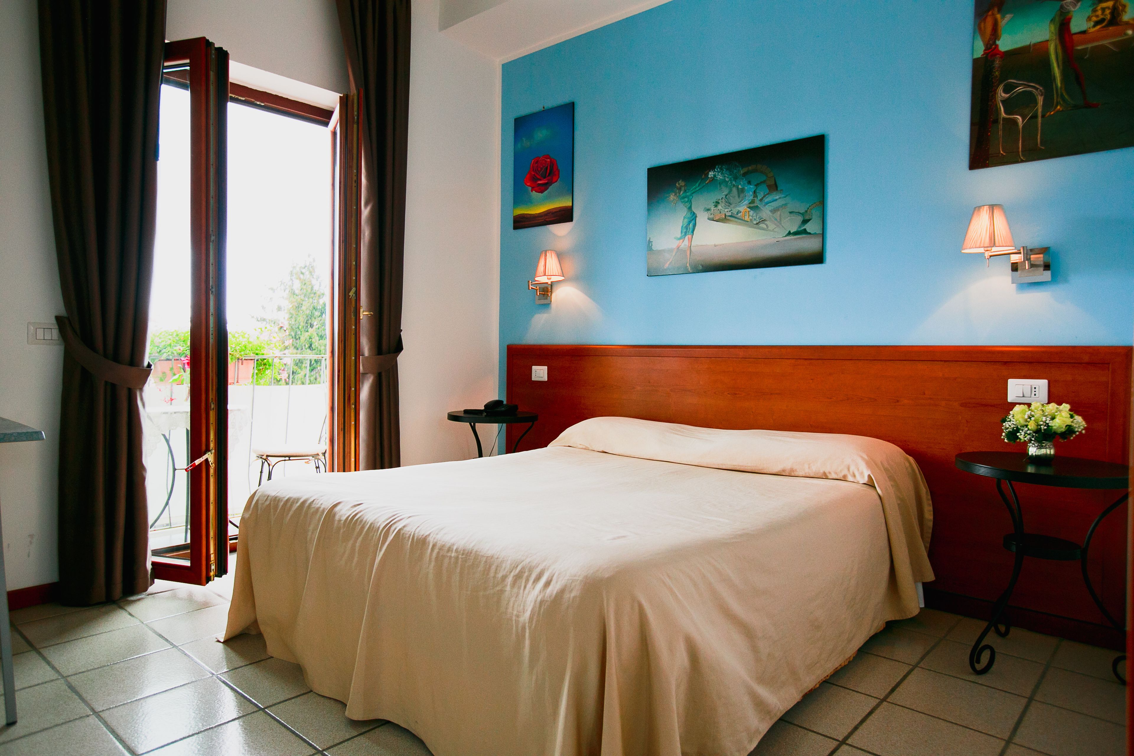 Una habitación de hotel con cama, una mesita de noche con lámpara y obras de arte en las paredes.