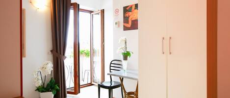 A hotel room with a bed, a dining table with chairs, a white wardrobe, and a potted orchid.