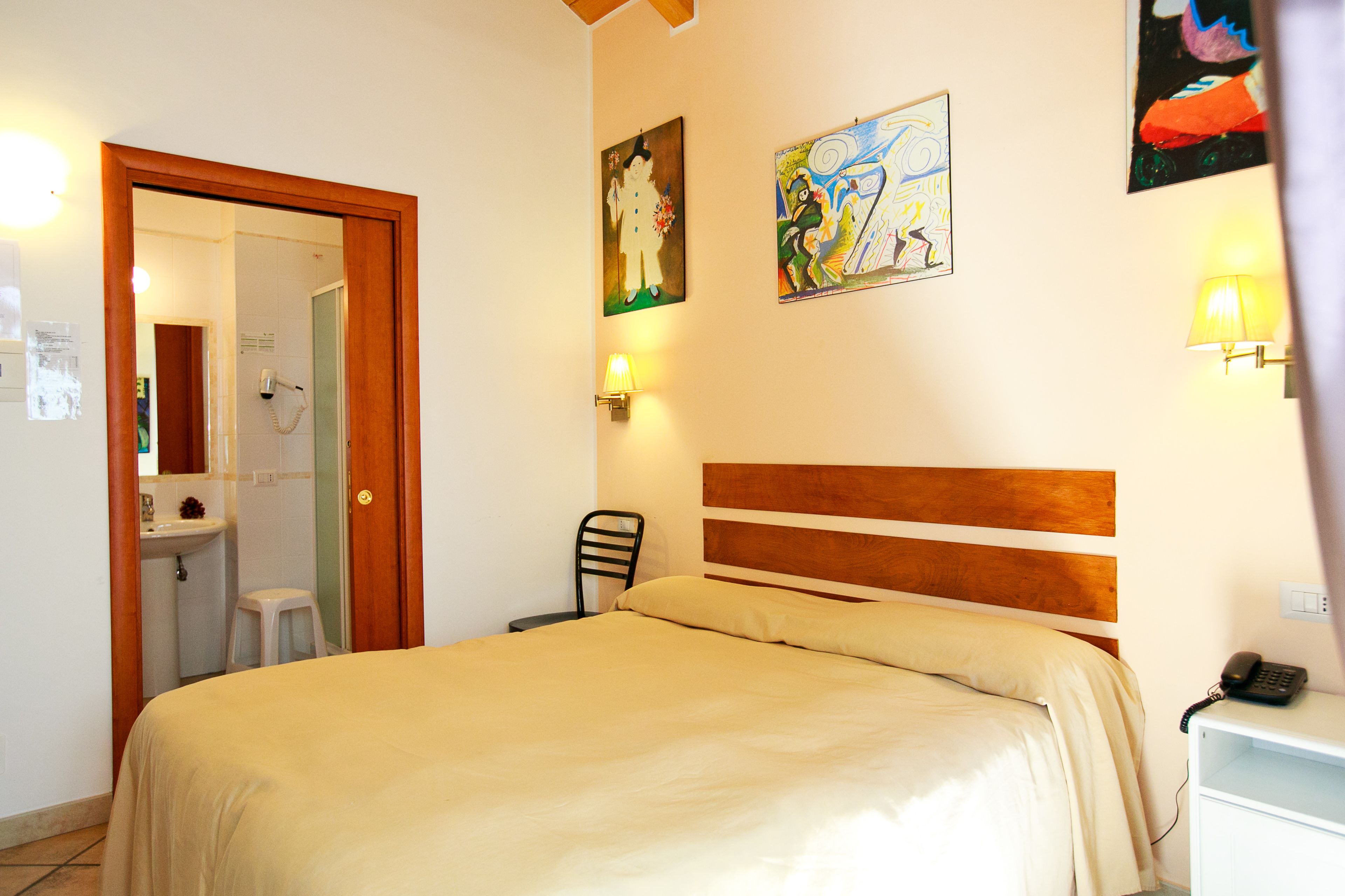 A hotel room with a bed, a chair, a nightstand, a lamp, a phone, and a bathroom visible through an open door.