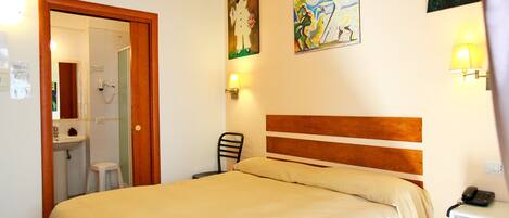 A hotel room with a bed, a chair, a nightstand, a lamp, a phone, and a bathroom visible through an open door.