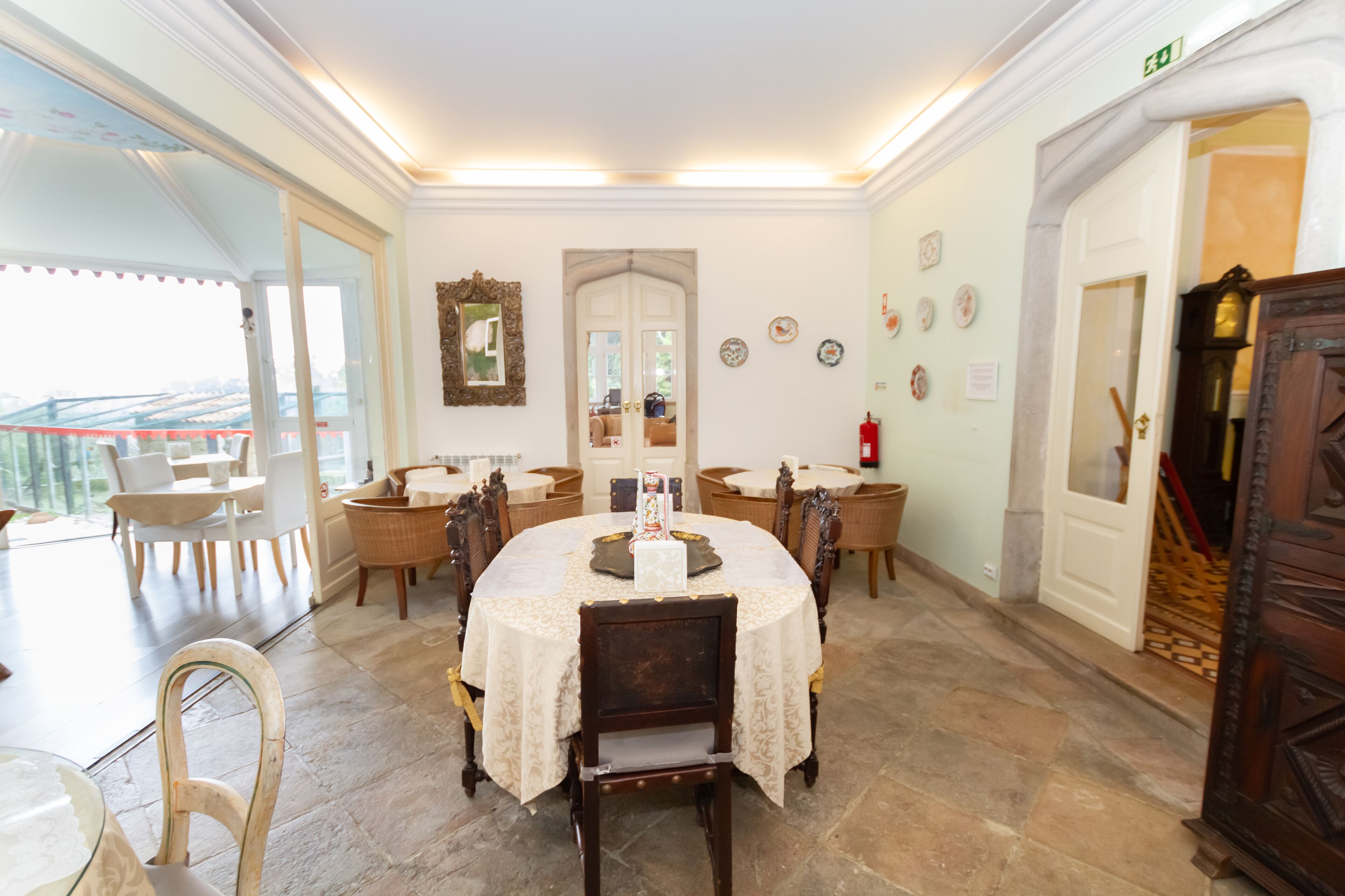 A dining area with a round table, chairs, and a buffet setup. There are doors leading to other rooms, and a fire extinguisher is visible.