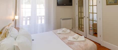 Hotellihuone, jossa on sänky, seinälle asennettu televisio, patteri ja lasipaneeleilla varustettu ovi.