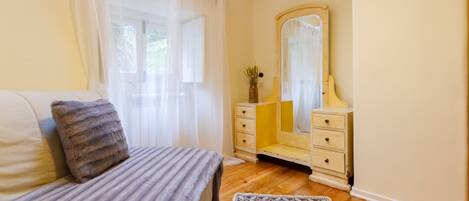 A bedroom with a bed, a dresser, a mirror, and a window with sheer curtains.