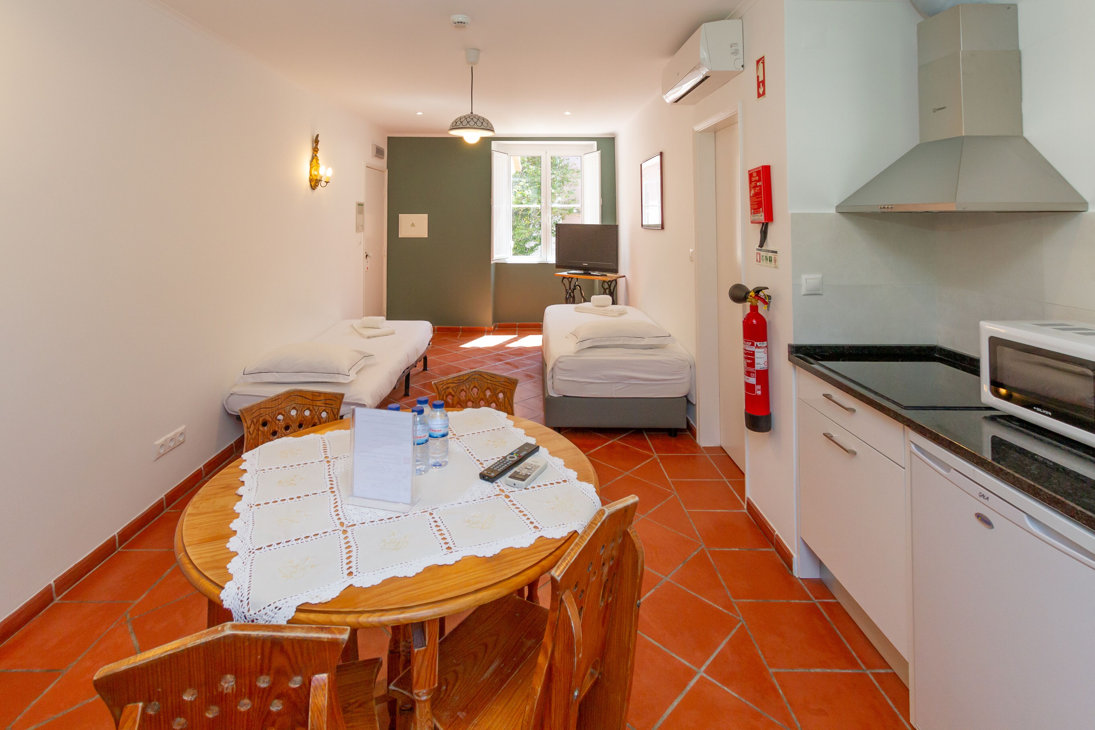 A compact hotel room with a dining area, kitchenette, and a bed.