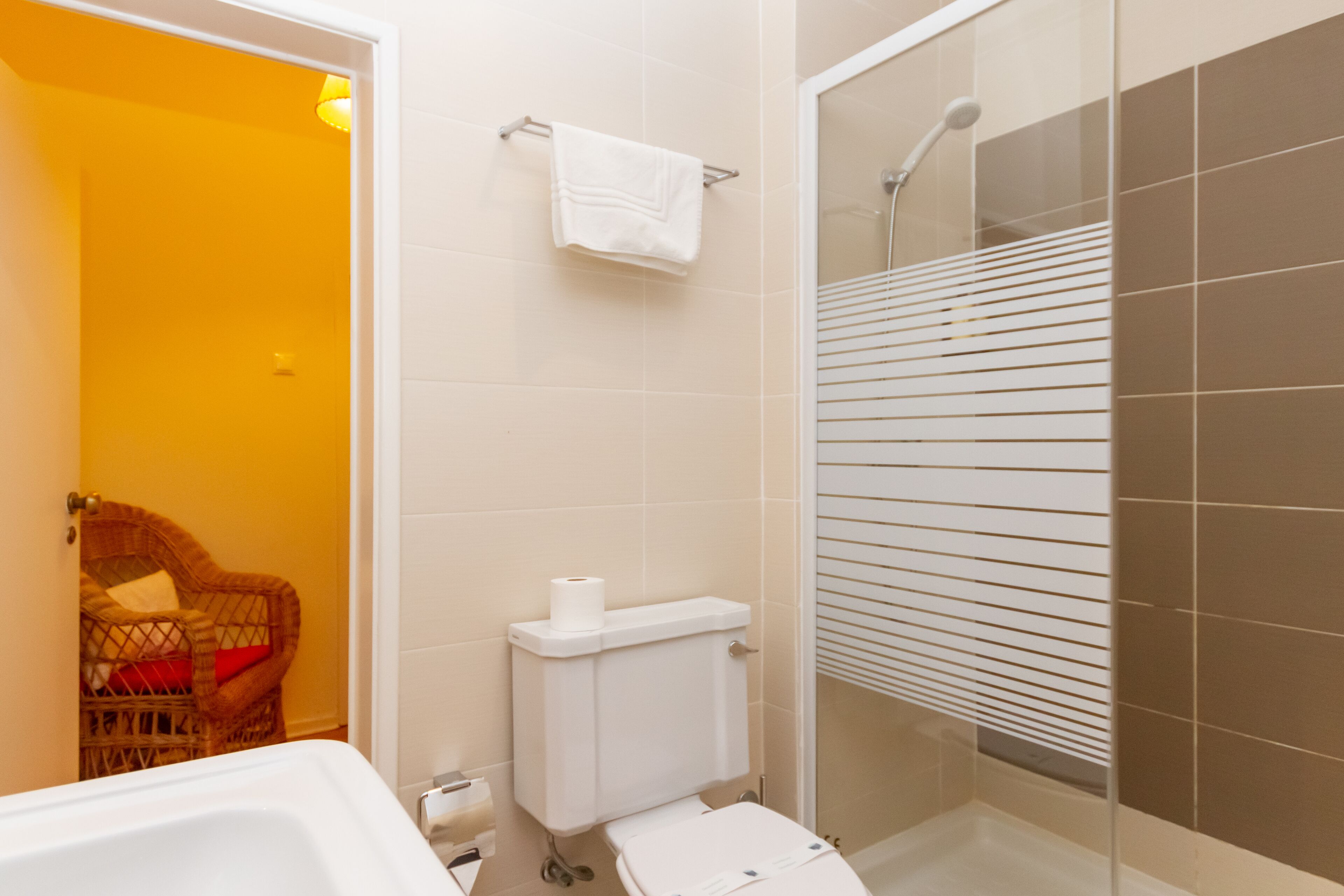 Un baño con inodoro, ducha y una silla de mimbre.