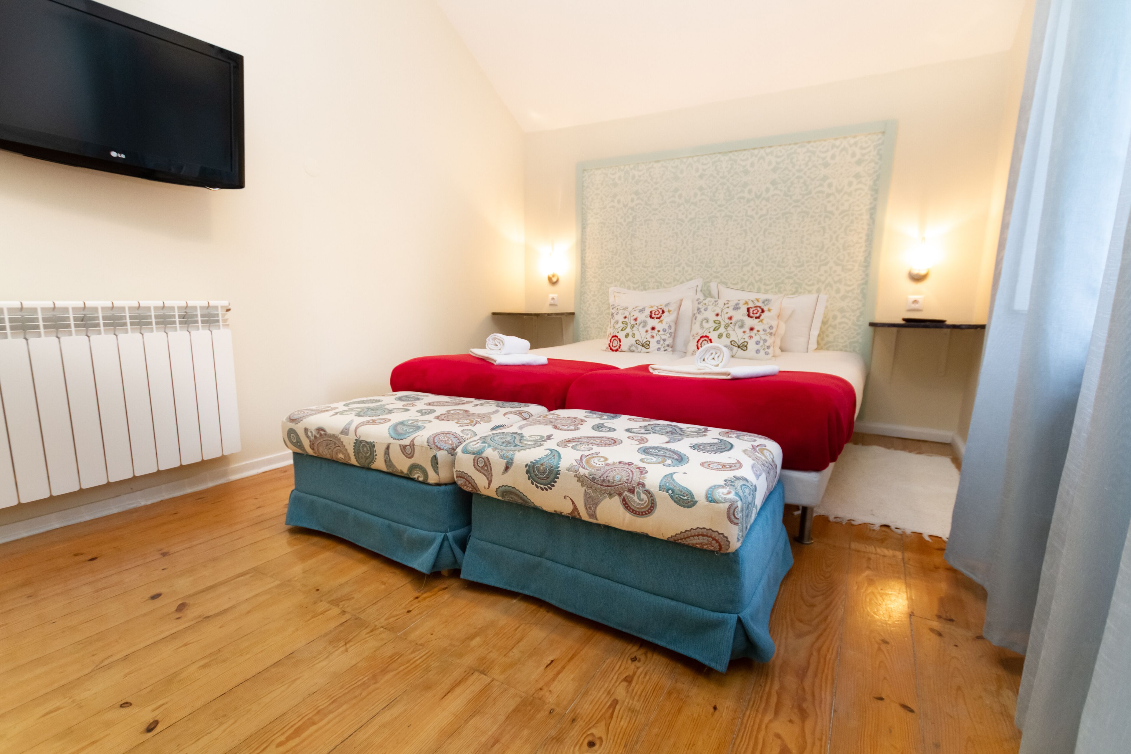 A bedroom with a bed, a TV mounted on the wall, and a radiator.