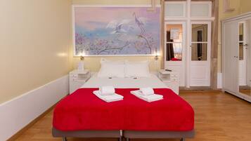 Habitación de hotel con una cama grande, una colcha roja, almohadas blancas y dos toallas dobladas con cuidado sobre la cama. En la pared, encima de la cama, hay un cuadro de pájaros.