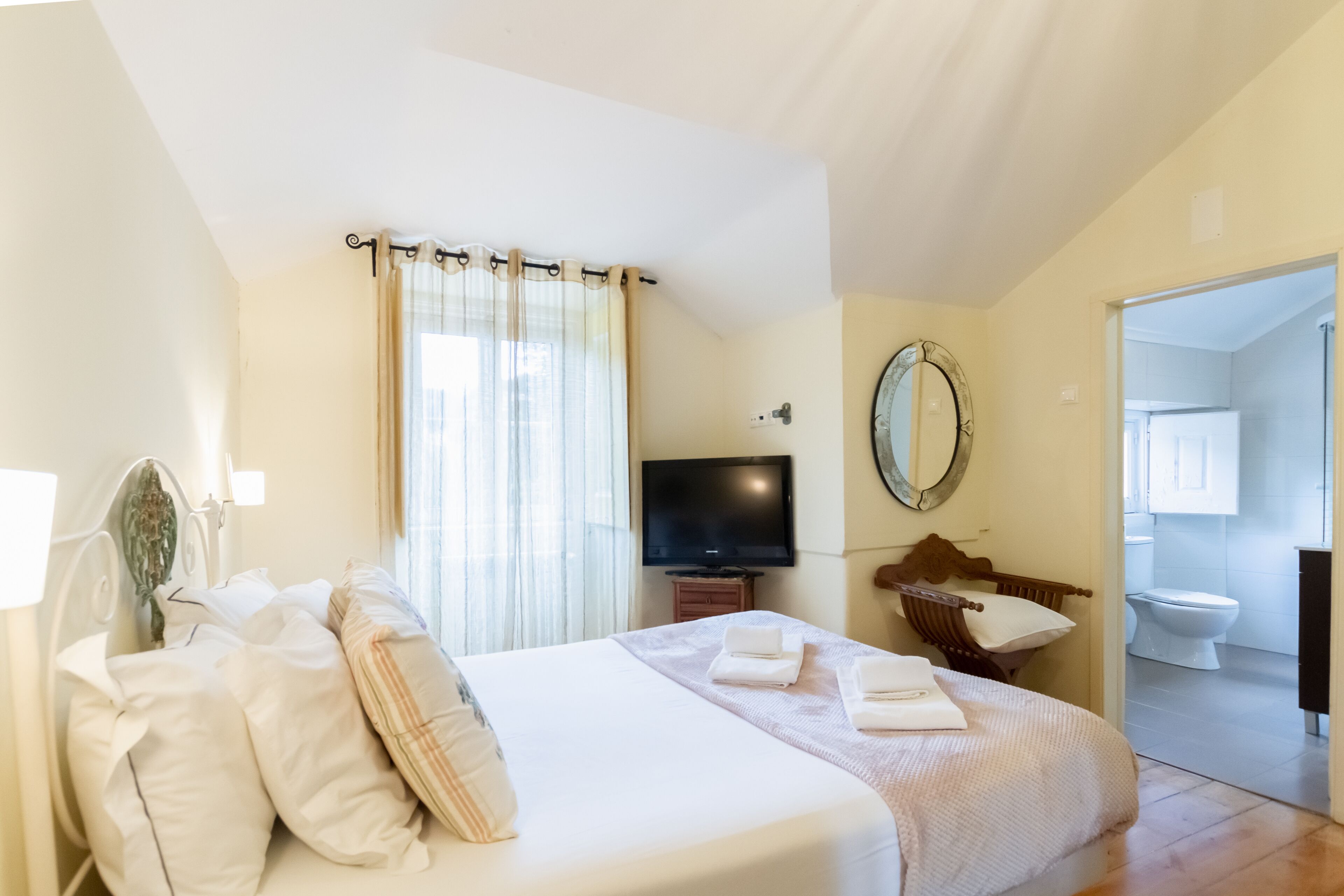Una habitación de hotel con cama, televisión, espejo y baño visible a través de una puerta abierta.