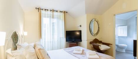 A hotel room with a bed, a television, a mirror, and a bathroom visible through an open door.