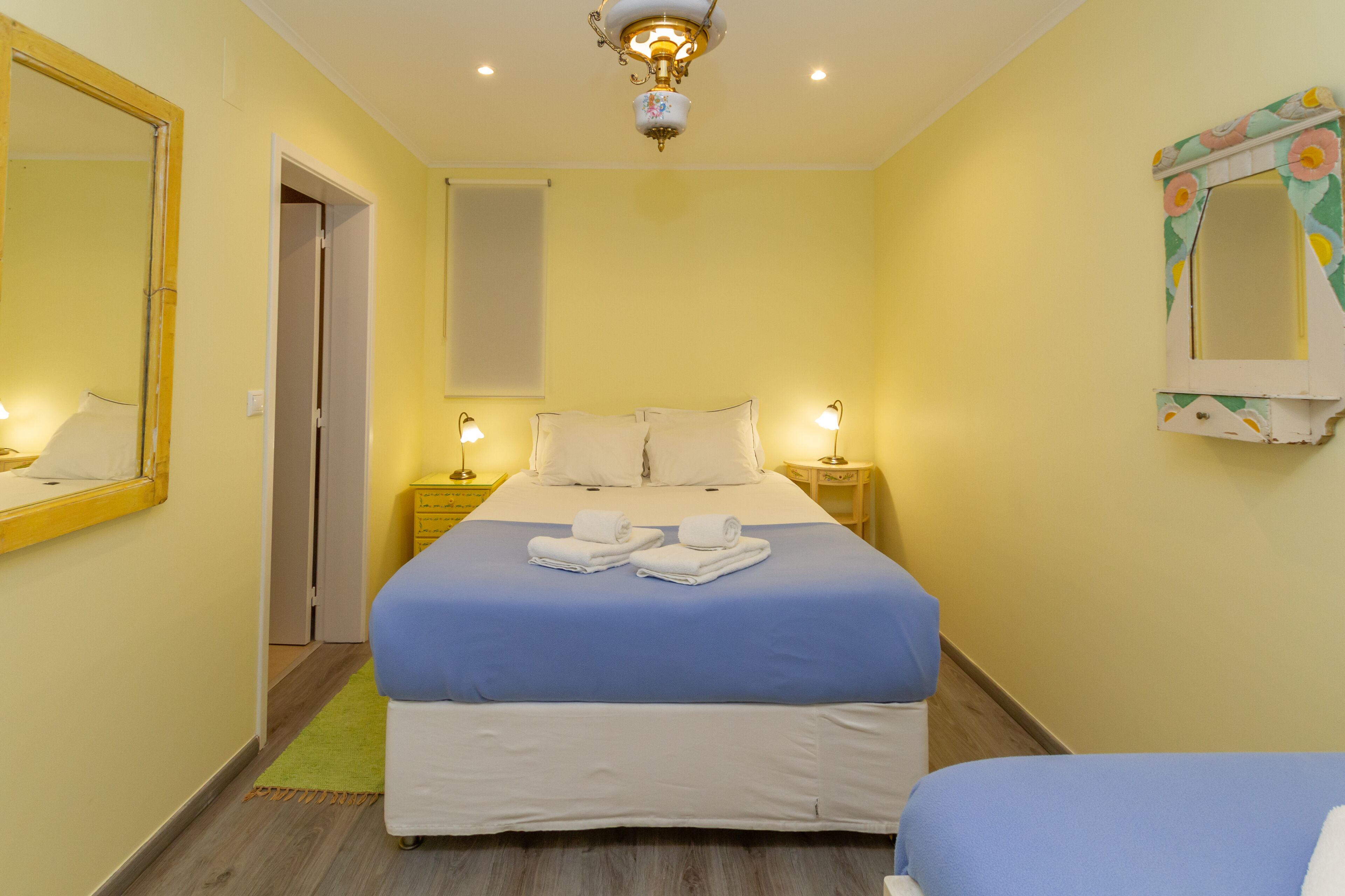 A hotel room with a bed, two bedside tables, a mirror, and a ceiling light fixture.