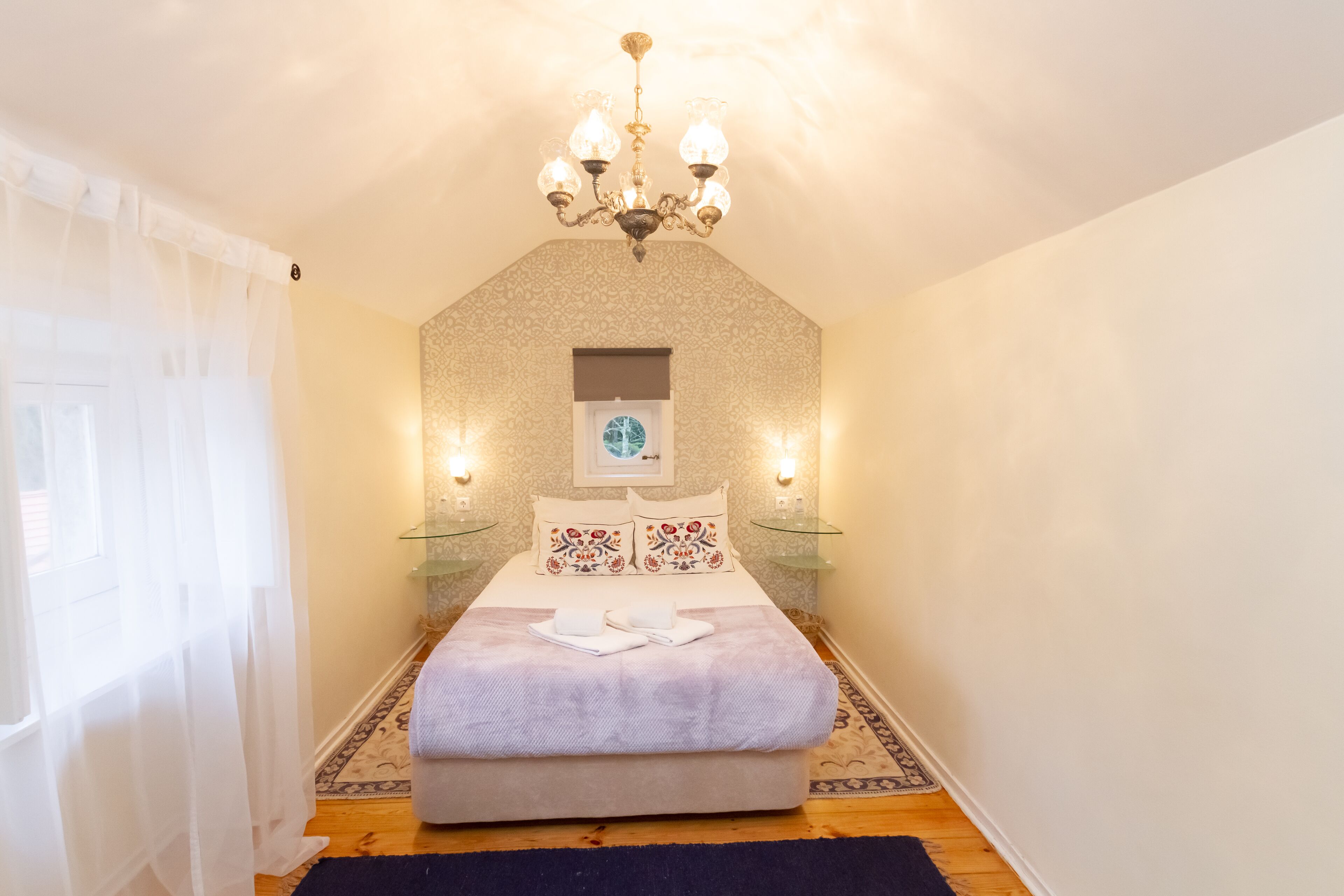 A bedroom with a bed, a chandelier, bedside tables, and a patterned wall.