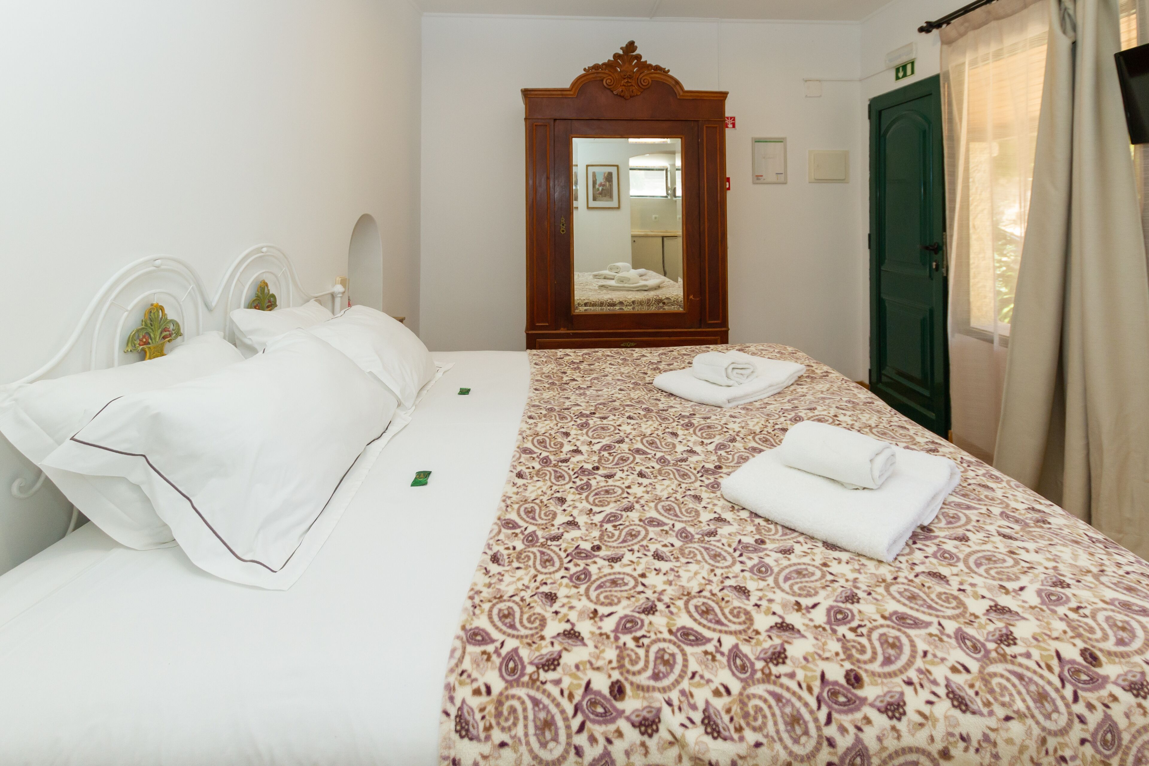 Habitación de hotel con cama, armario, espejo y puerta verde.