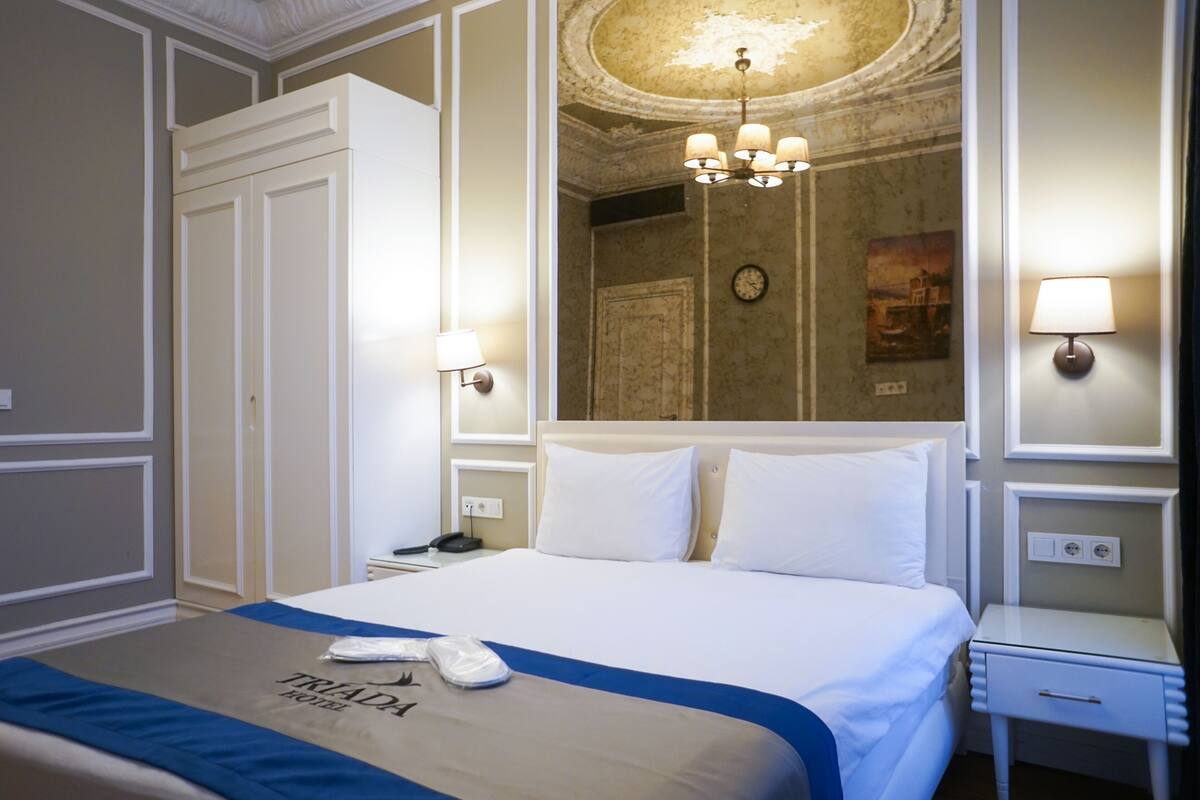 A hotel room with a large bed, a nightstand, a lamp, a clock, and a painting on the wall.